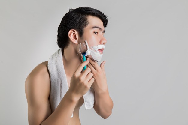 Seorang pria dengan handuk di bahunya sedang mencukur kumis dan jenggot